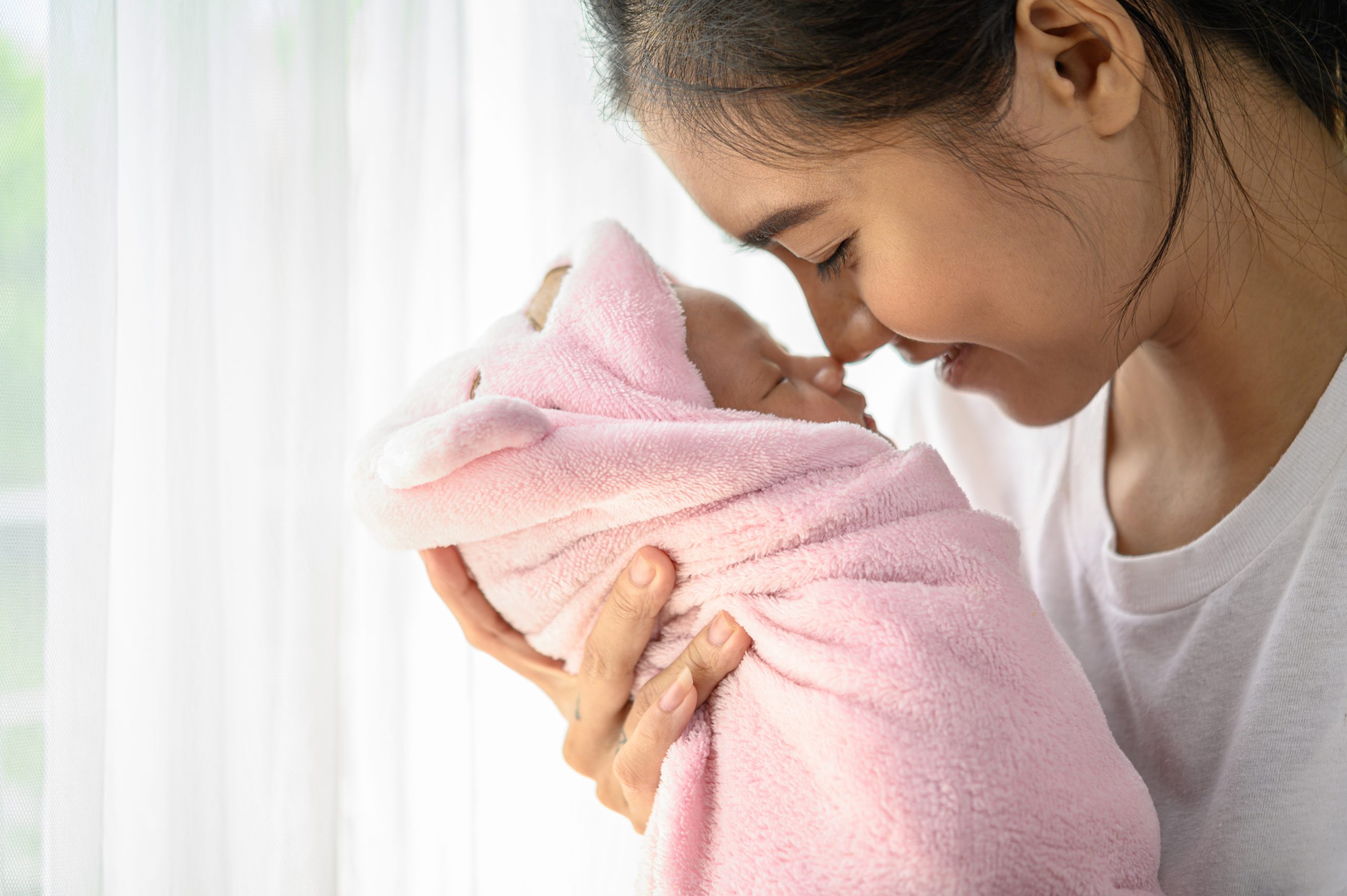 The newborn baby sleeping in the hands of the mother and their noses touching